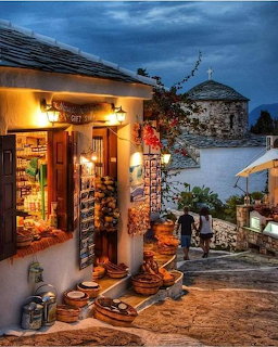Warmly lit shop on a stone street in Alonnisos Island village at dusk with two people walking