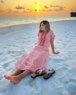 Woman in a pink dress sitting on white sand at the beach during sunset