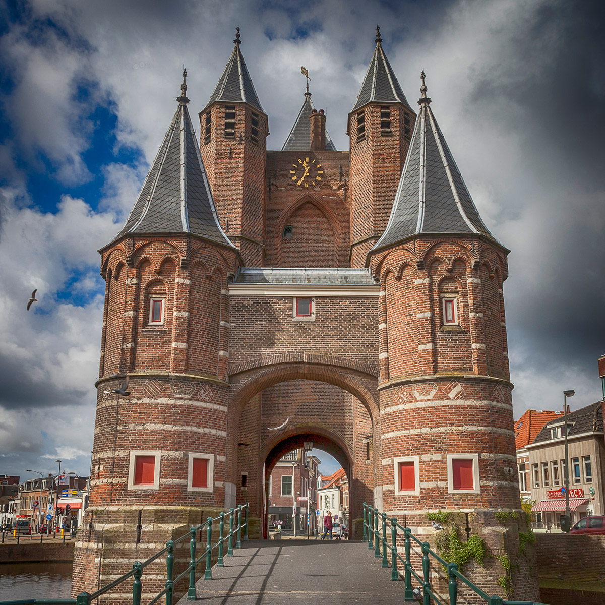 Medieval brick gate tower with two pointed turrets and arched passage under cloudy sky