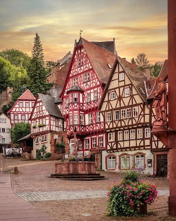Half-timbered houses with red and white facades around a coblestone square with fountain in Miltenberg