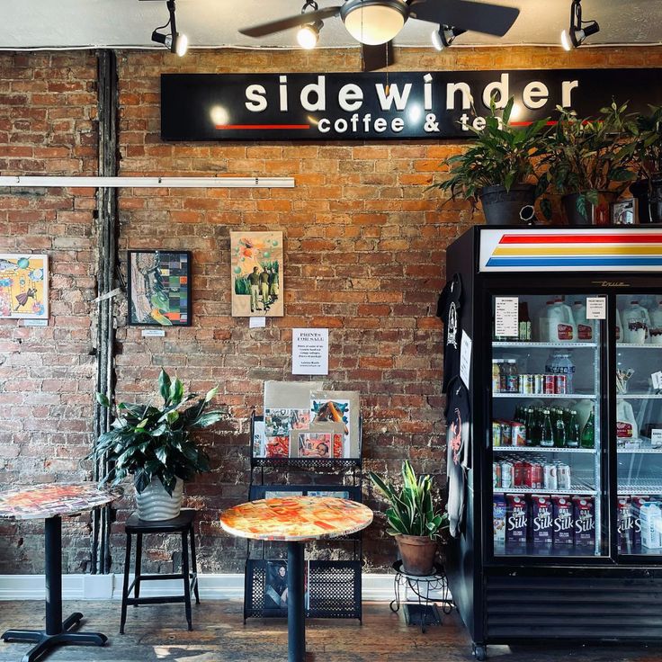 Coffee shop interior with brick wall, Sidewinder sign, small tables, plants, and a drink refrigerator