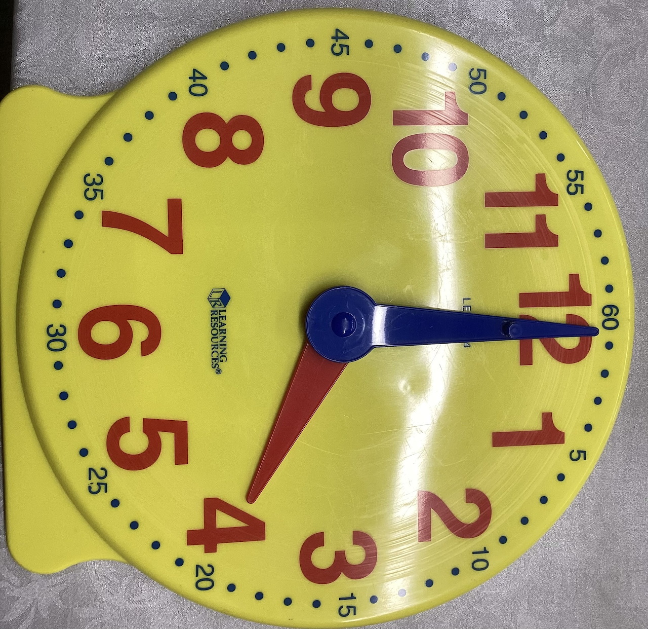 Yellow toy clock with red numbers and blue and red hands
