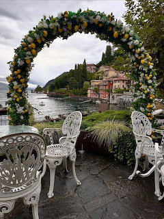 Floral arch and white garden chairs on terrace overlooking Italian lakeside village