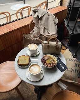 Marble café table with two lattes, cake slice, granola bowl, handbag and coat on bench