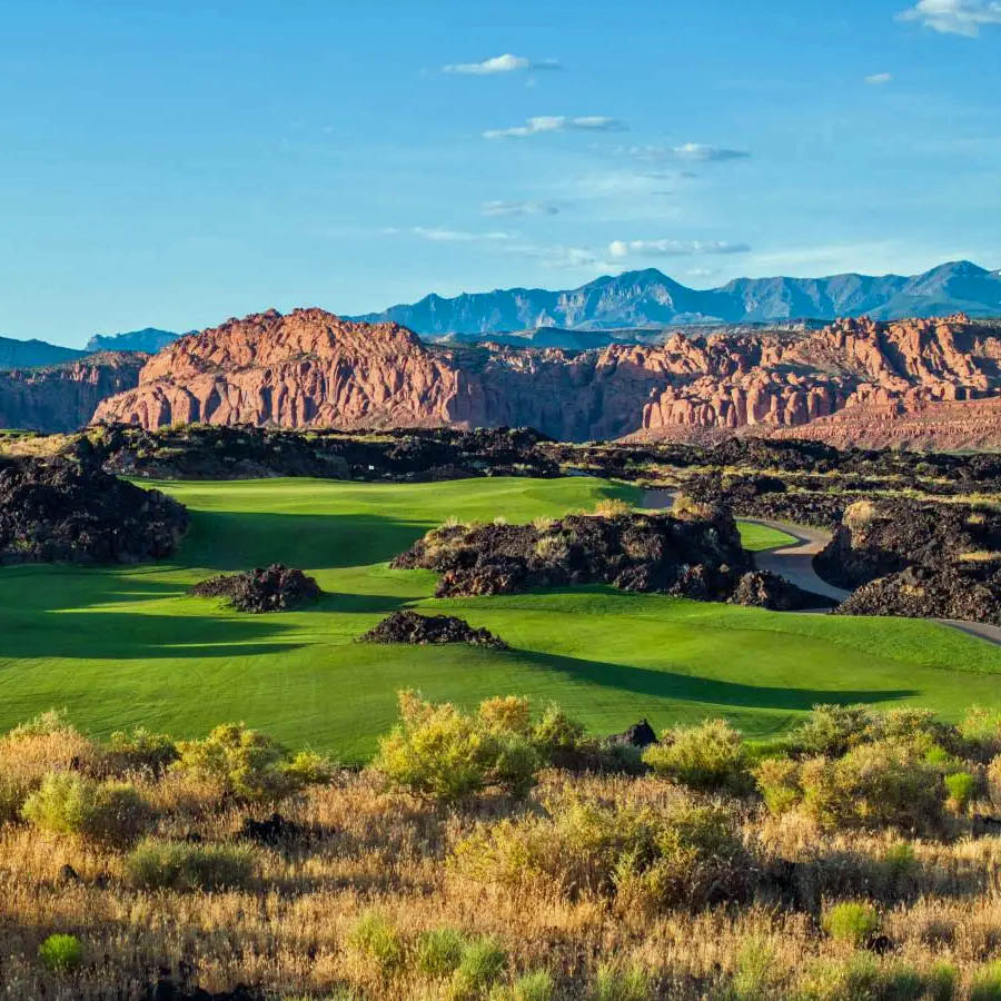Lush green golf course fairways surrounded by desert terrain with red rock cliffs and mountains in background