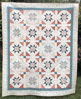 Handmade quilt with white star pattern blocks, coral accents, and blue border hanging outdoors