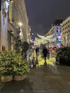 London street at night decorated with Christmas lights and trees, people walking on wet pavement