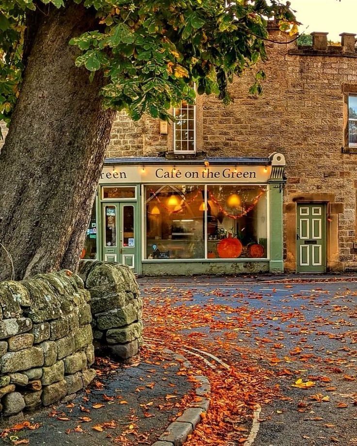 Stone cafe with warm interior lights on an autumn village street covered in orange fallen leaves