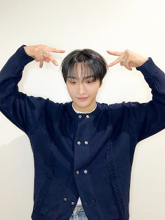 Young man in navy cardigan making peace signs above his head against white background