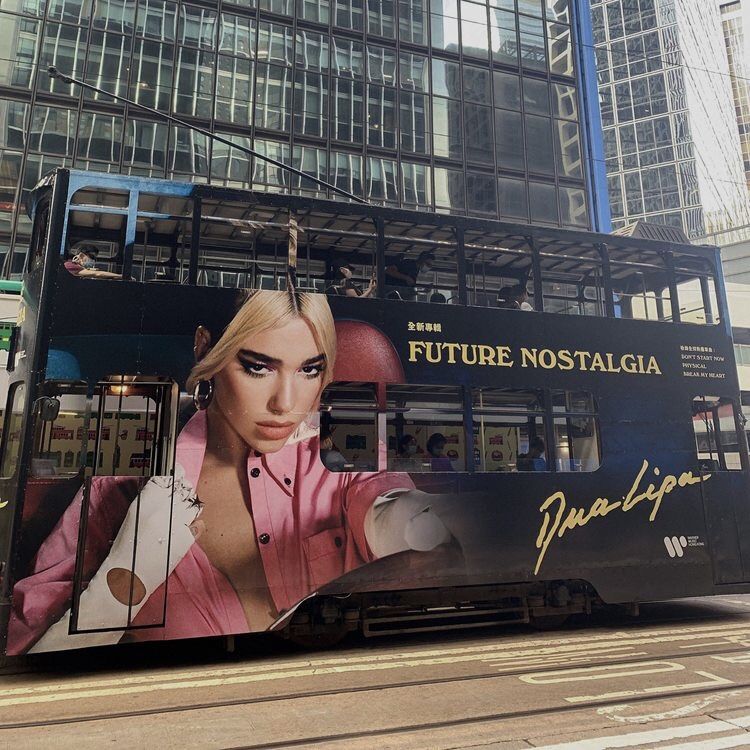 Double-decker bus with Dua Lipa album wrap parked on city street