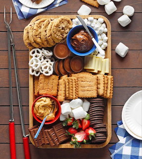 S'mores charcuterie board with chocolate, marshmallows, graham crackers, cookies, and strawberries on wood