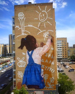 Street art mural of girl in blue dress drawing sun and flowers on building wall