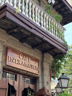 Stone building exterior of Cafe Intramuros with wooden sign, balcony with white balusters, and street lamp