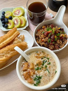 Overhead view of Asian breakfast with congee, fried dough sticks, fried rice, fruit plate, and tea