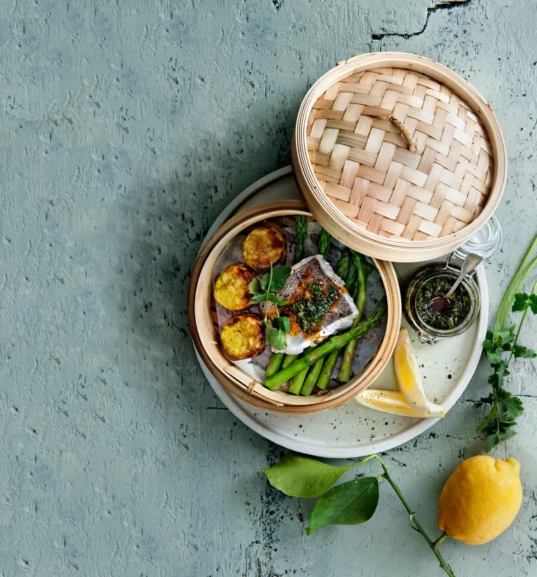 Top view of steamed hake with green asparagus, potatoes, herbs, and lemon on a plate