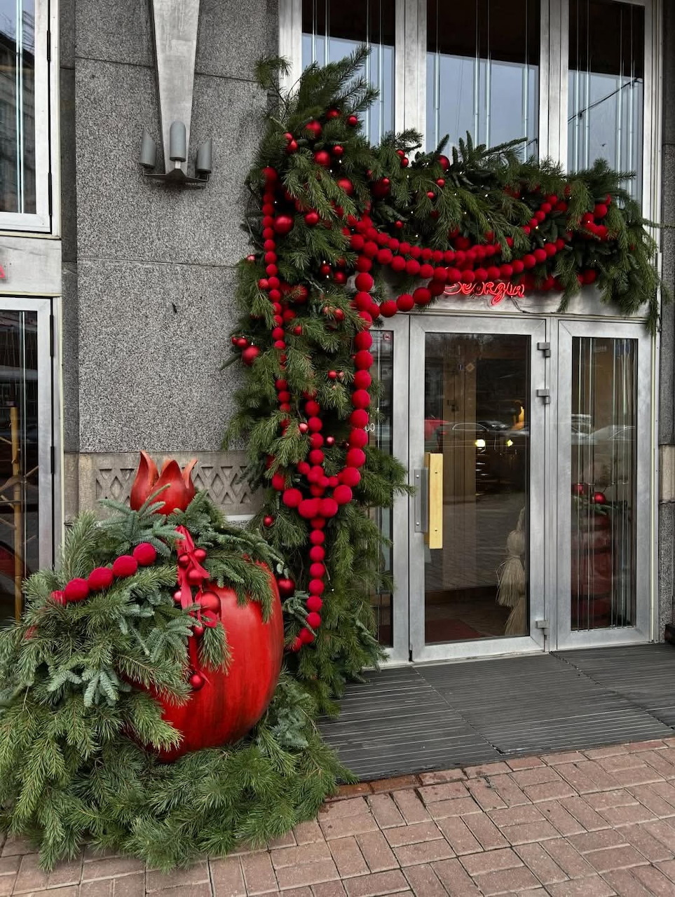 Building entrance decorated with Christmas garlands, red ornaments, and a large red bauble