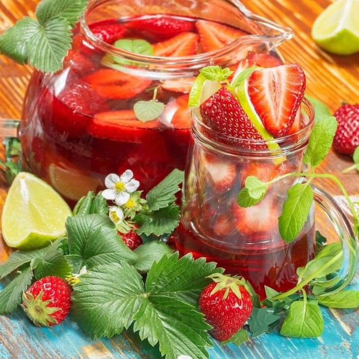 Strawberry infused water in glass containers with mint, lime, and fresh strawberries on wooden table