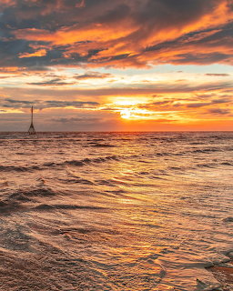 Sunset over rippling ocean water with orange clouds and a distant marker on the horizon