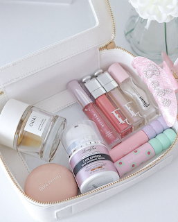 White cosmetic case open displaying pastel skincare and beauty products with a flower vase behind