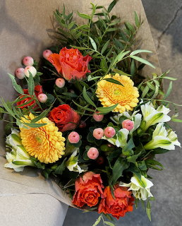 Colorful bouquet with orange roses, yellow flowers, white lilies and pink berries in brown paper wrap