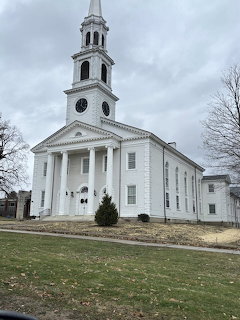 White church building with a tall steeple under an overcast sky