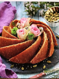 Chocolate bundt cake topped with pink roses and pistachios on a slate plate