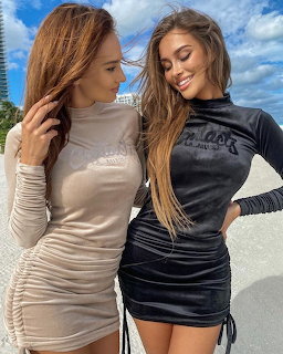 Two smiling women in tight velvet mini dresses posing together outdoors
