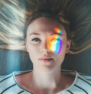 Young woman with blonde hair and rainbow light prism on face