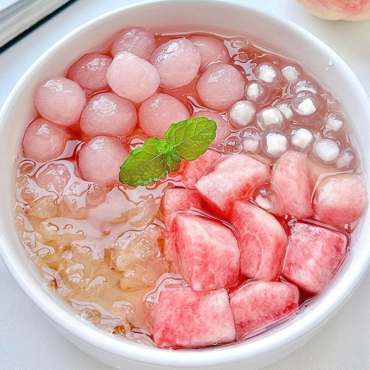 Bowl of peach jelly dessert with tapioca pearls, sago, and mint leaf garnish