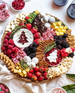 Overhead view of a round Christmas charcuterie board with fruits, cheese, crackers, and holiday decorations