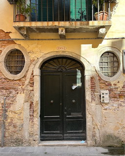 Old weathered facade with black double door, round windows, and balcony