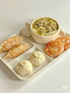 White tray with a bowl of Korean-style soup, steamed buns, and pastries on a white background.