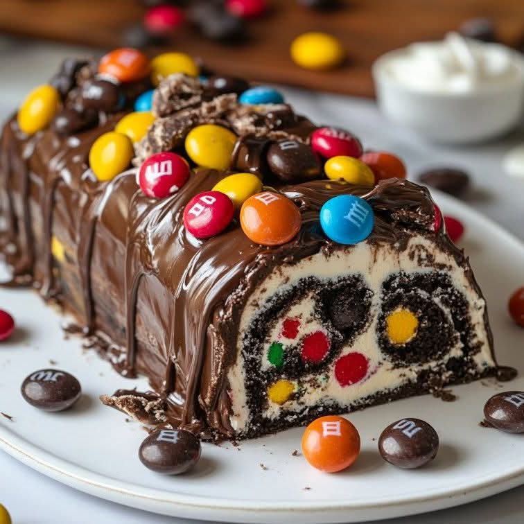 Sliced chocolate cake roll with candy pieces, covered in chocolate ganache and colorful candies on a white plate