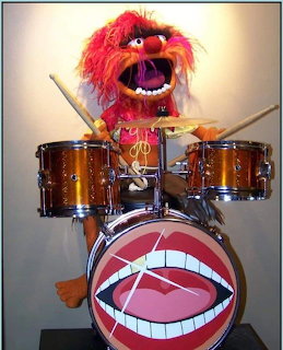 Red puppet drummer playing a drum set with a mouth design on the bass drum