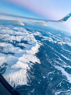 Airplane wing seen from a window above snow-covered Rocky Mountains