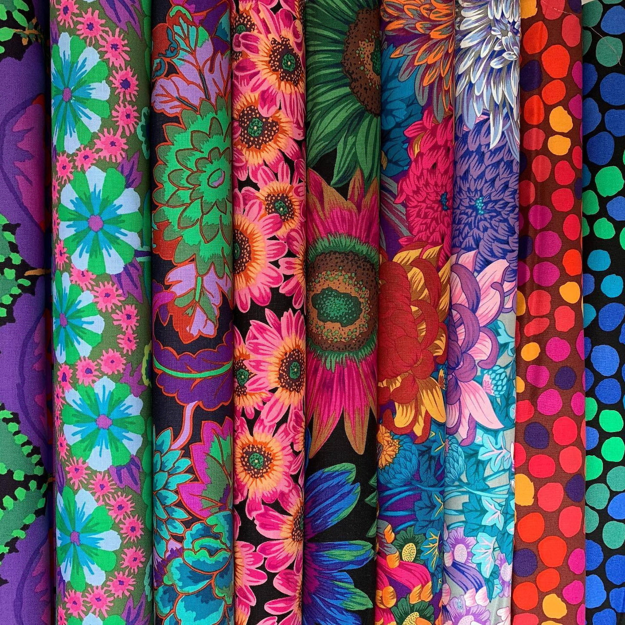Vertical stack of colorful patterned fabric rolls with floral and geometric designs