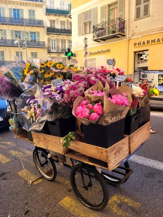 Wooden cart on bicycle wheels filled with bouquets of pink, yellow, and purple flowers on a city street