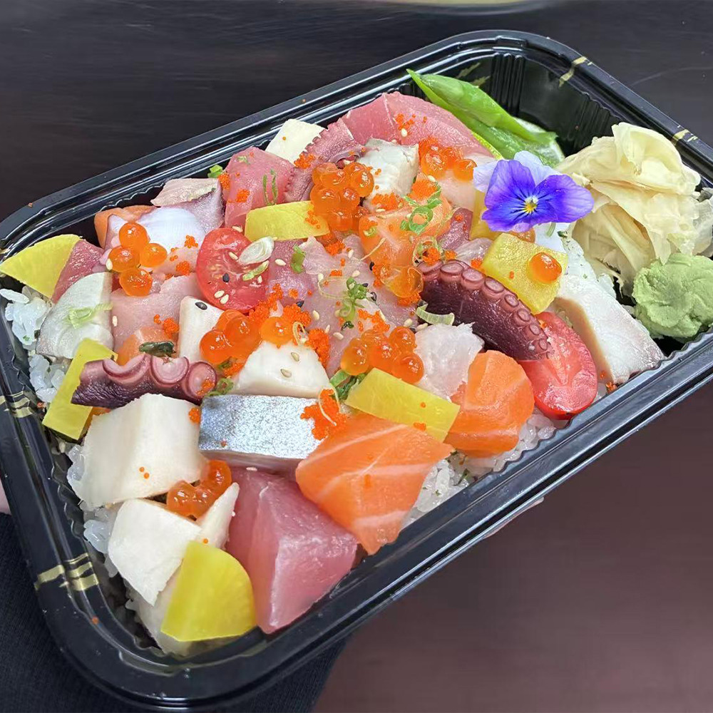 Takeout sashimi tray with assorted raw fish, salmon roe, octopus, and edible flowers on rice