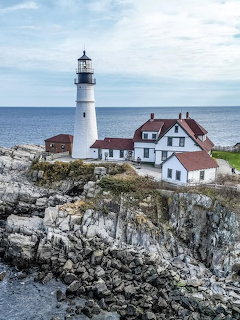 White lighthouse and keeper's house on rocky Maine coastline with ocean view