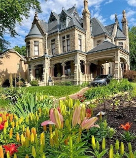 Victorian-style inn behind a colorful flower garden with blooming lilies and greenery