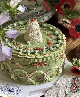 Multi-tiered green cake with ornate floral piped icing decoration and small figurines