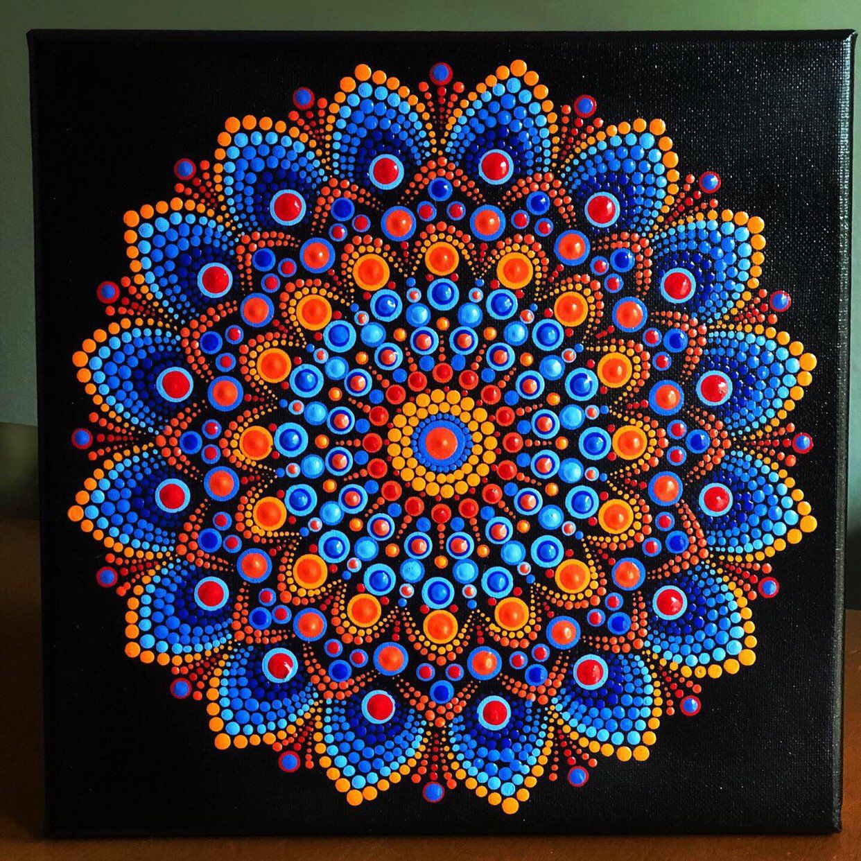 Colorful dot mandala with blue and orange petals radiating from yellow center on black background