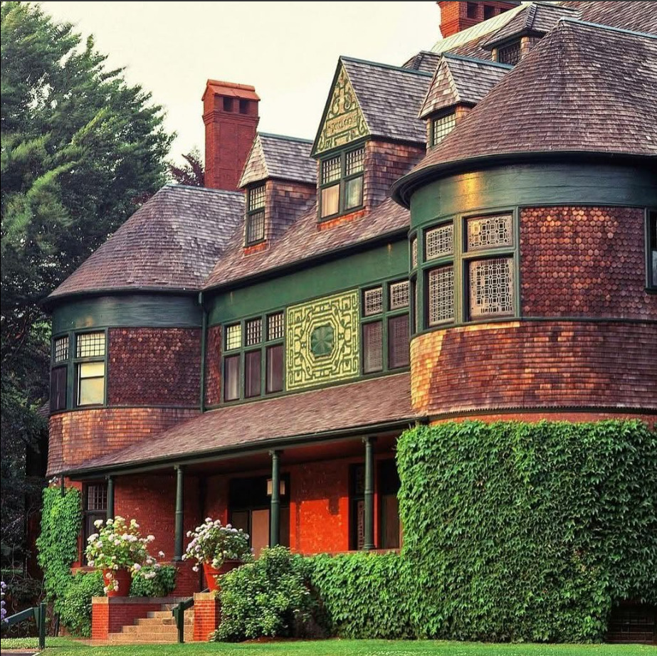 Large old brick house with steep roofs, bay windows, and green hedges