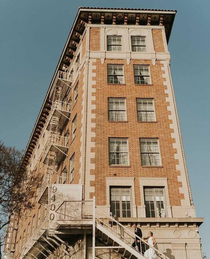 Tall multi-story brick hotel building with whitetrimed windows and fire escape viewed from below