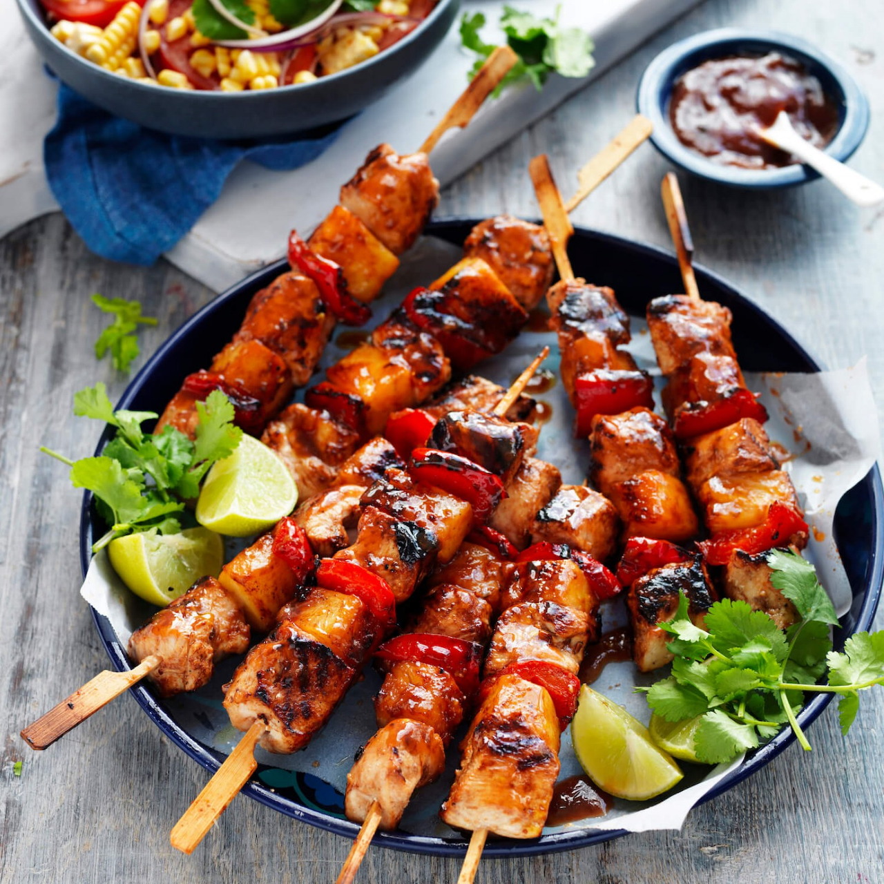 Glazed grilled meat skewers with lime wedges and cilantro on a dark plate