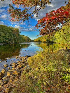 Lake surrounded by vibrant autumn trees with red and orange leaves reflecting in still water under cloudy blue sky