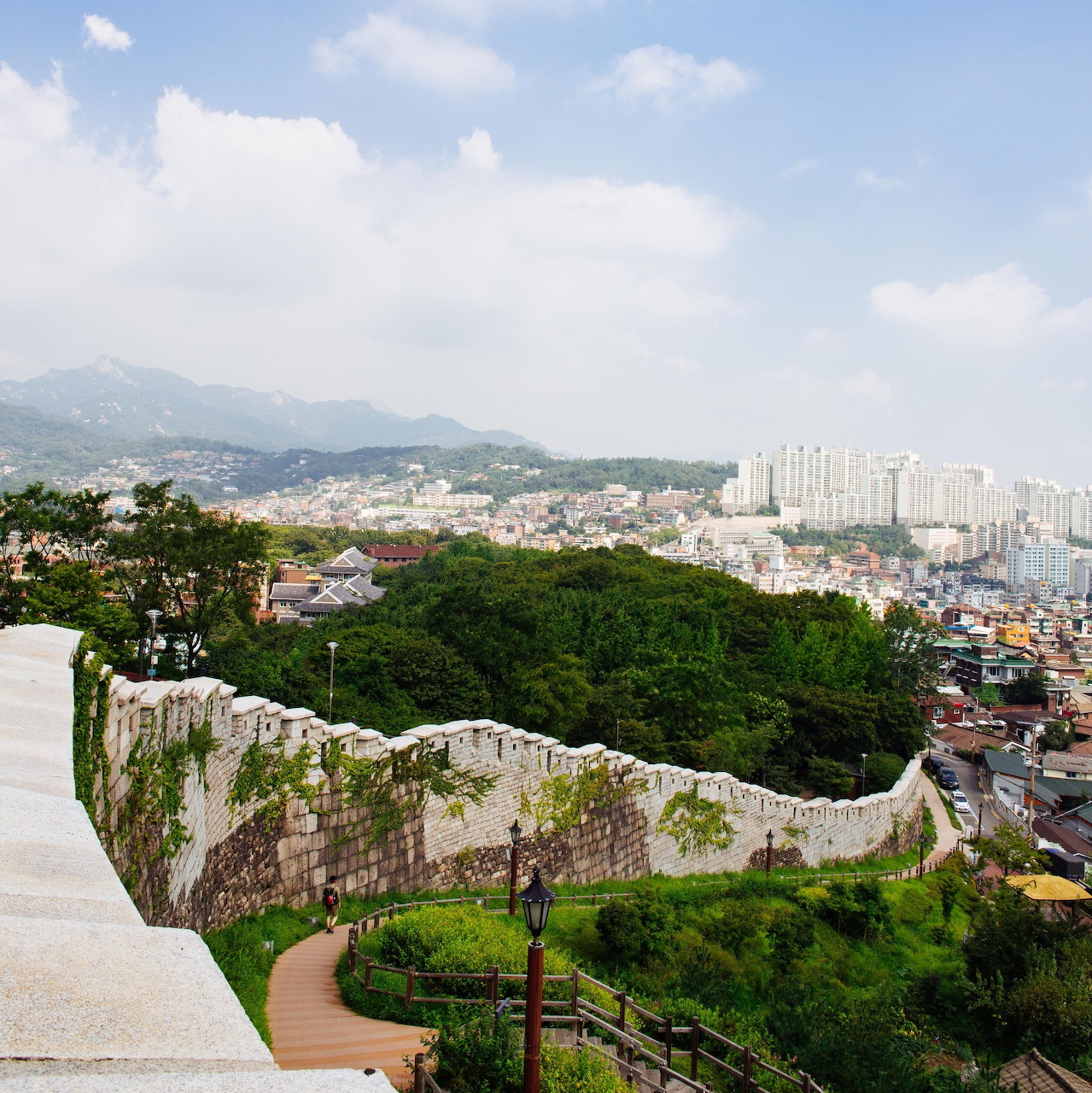 Panoramic view of Seoul cityscape from elevated garden terrace with curved stone wall and lush greenery