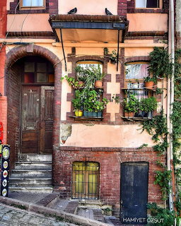Rustic peach and brick building with wooden door, stone steps, and plants on balconies