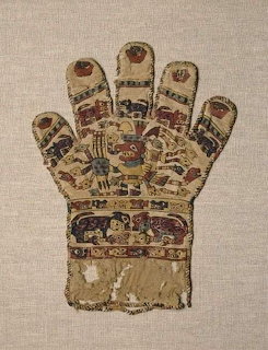 Ancient woven textile glove with colorful Peruvian-style figures and animal motifs on linen background