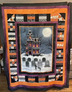 Halloween quilt with haunted house, gravestones, full moon, and orange-black patchwork border